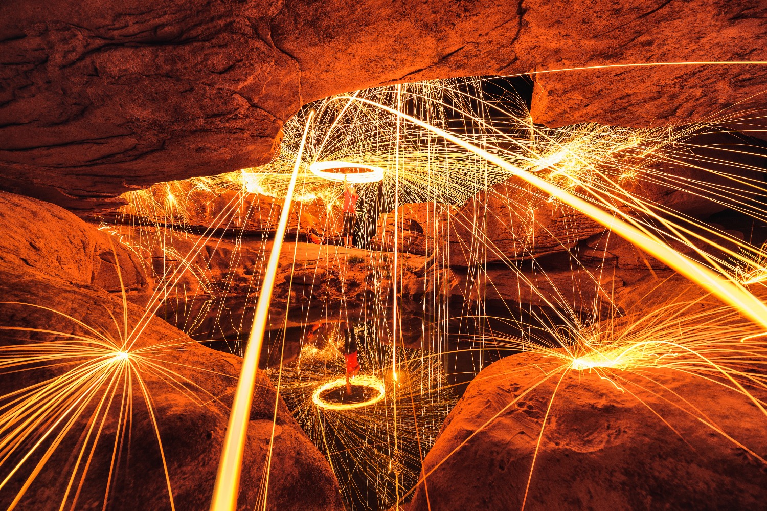 man-wielding-spark-fire-swirl-stone-hole-cave-pond-reflection-night-sam-phan-bok.jpg